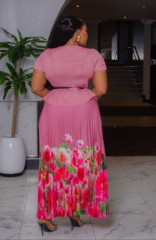 Model wearing Blossom Beauty mauve pink Miyake pleated two-piece set featuring a floral peplum top, pearl buckle belt, and flowing pink rose-print maxi skirt.