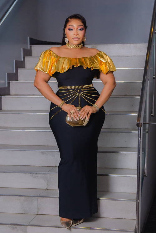 Black and gold off-shoulder bandage maxi dress with metallic gold ruffle neckline and decorative gold beadwork at the waist.