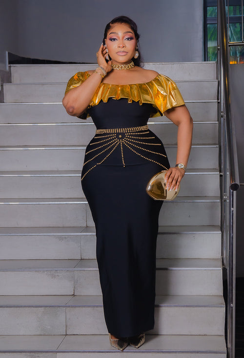 Black and gold off-shoulder bandage maxi dress with metallic gold ruffle neckline and decorative gold beadwork at the waist.