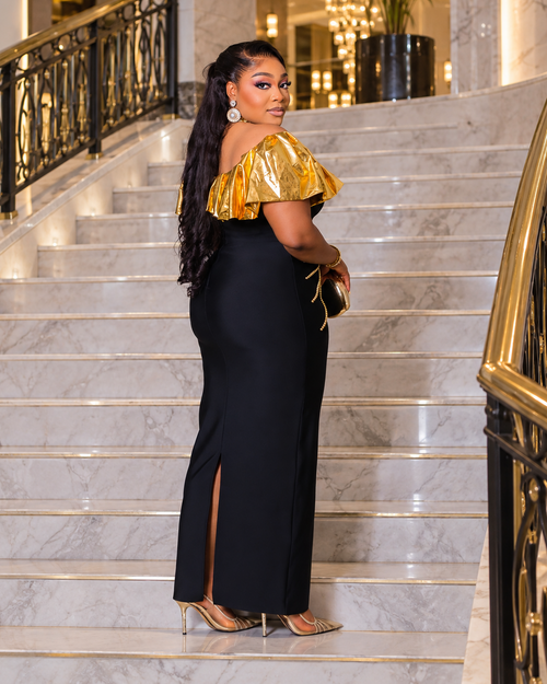 Black and gold off-shoulder bandage maxi dress with metallic gold ruffle neckline and decorative gold beadwork at the waist.