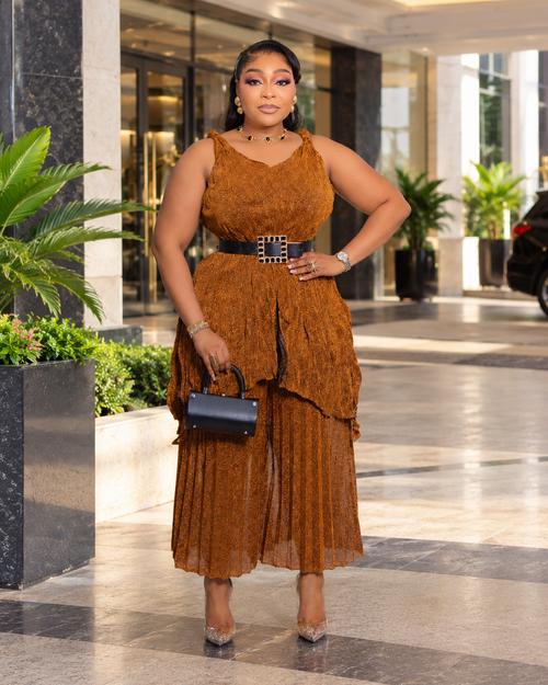 Model wearing Serena Shimmer copper brown Miyake pleated two-piece set featuring a sleeveless top and matching shimmering capri pants.